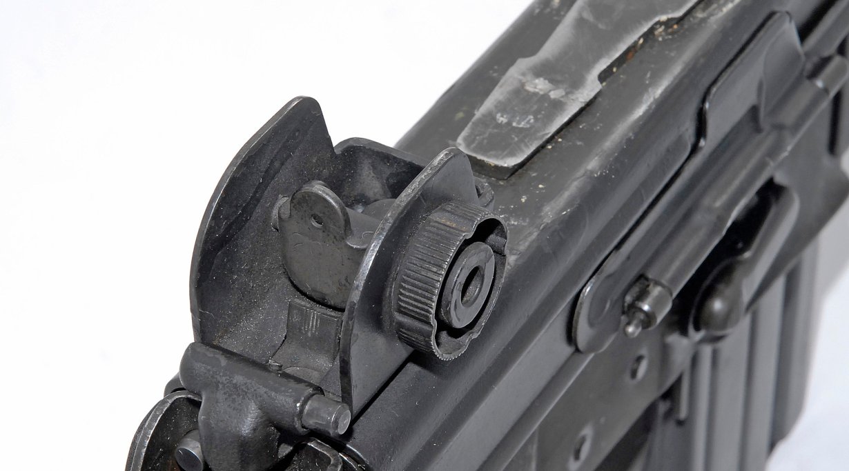 La tacca di mira è più simile a quella dell'M1 Garand o della Carabina M1, ma puo' essere regolata solo in deriva. Invece della ghiera forata che troviamo sulla mira A1 dell'M16, che richiedeva la punta di una cartuccia per essere azionata, qui abbiamo una più comodo pomello. Nella foto si vede anche parte della slitta portaottiche proprietaria.